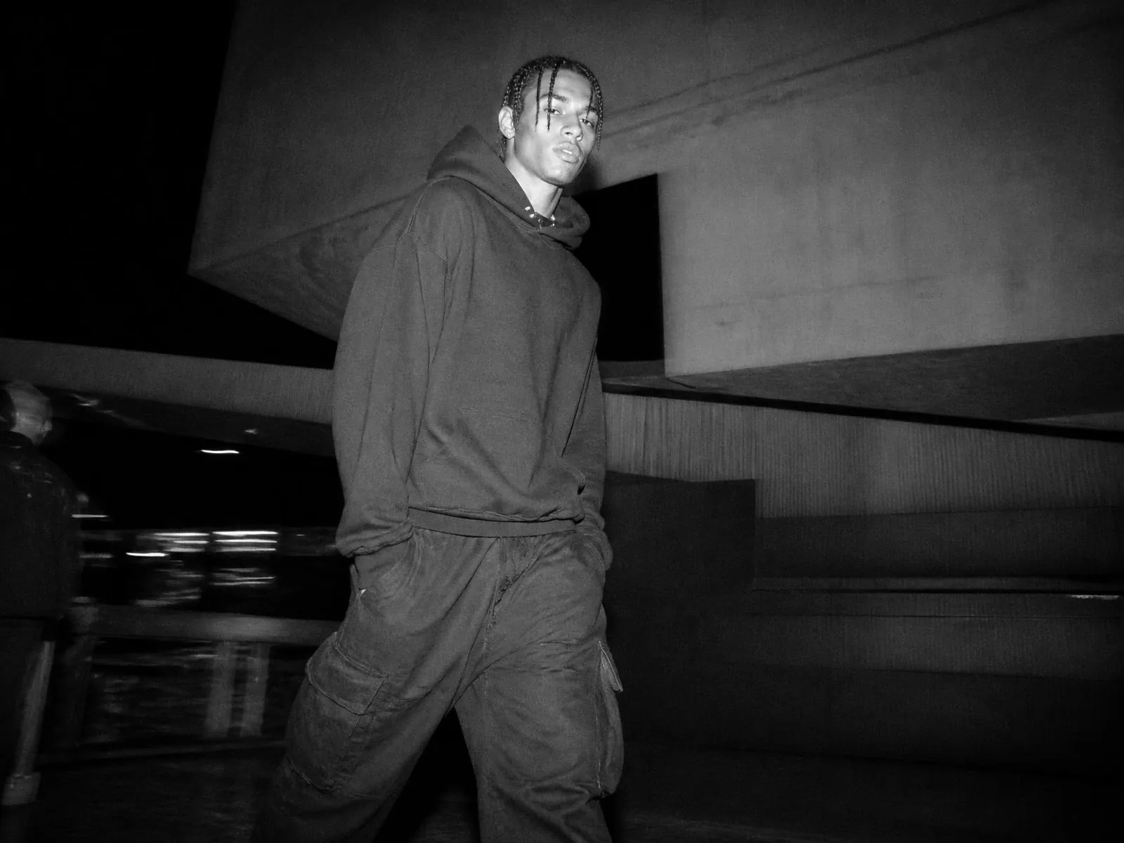 Model in a heavyweight hoodie in a concrete car park at night